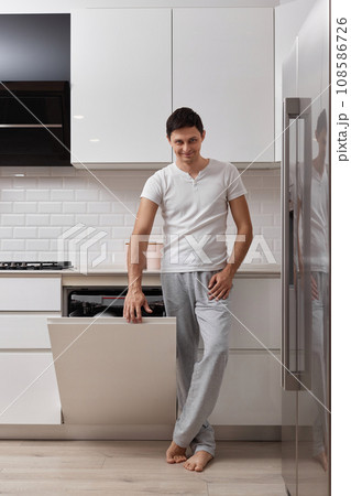 handsome husband man using dishwasher and washing dishes in white modern kitchen handsome husband man using dishwasher and washing dishes in white modern kitchen 108586726