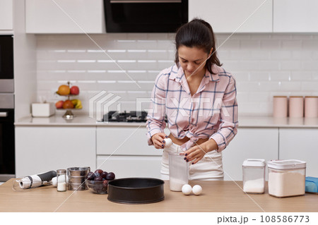 woman preparing dough and cracking eggs in bowl at kitchen woman preparing dough and cracking eggs in bowl at kitchen 108586773