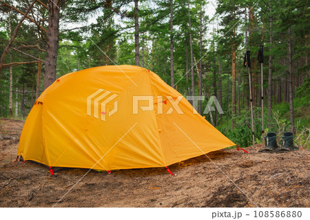 Hiking tourism adventure. Camping picnic orange tent campground in outdoor hiking forest. Touristic boots near camping tent. Campsite in nature at summer trip camp. Trekking travel vacation concept 108586880