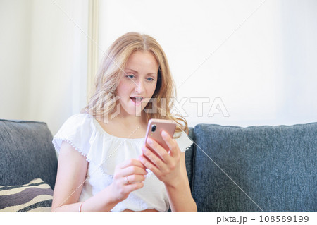 ソファーに座りスマホを操作する白人女性(喜び) ソファーに座りスマホを操作する白人女性(喜び) 108589199