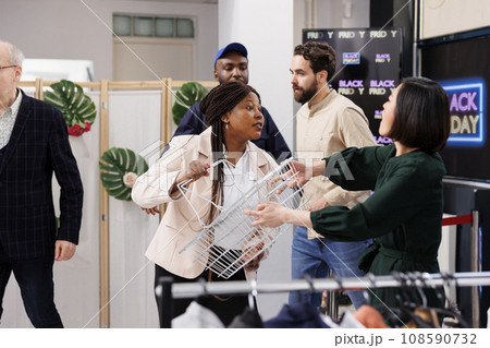 Mad angry diverse women customers arguing in clothing store, fighting for shopping basket during big sales in fashion boutique. Aggressive consumer behavior and Black Friday concept Mad angry diverse women customers arguing in clothing store, fighting for shopping basket during big sales in fashion boutique. Aggressive consumer behavior and Black Friday concept 108590732