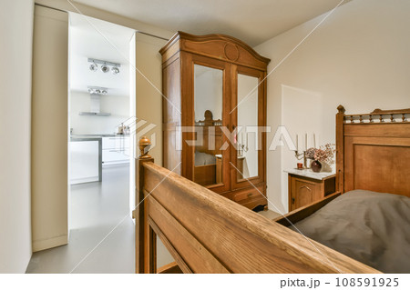 a bedroom with a bed, dresser and mirror on the wall in front of the door that leads to another room a bedroom with a bed, dresser and mirror on the wall in front of the door that leads to another room 108591925