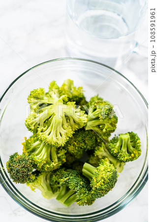 Measured ingredients in glass mixing bowls to prepare steamed broccoli. 108591961