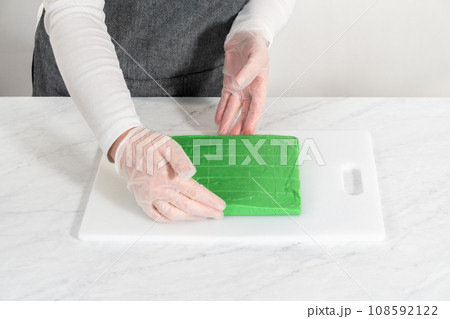 Cutting green fudge with a large kitchen knife into square pieces on a white cutting board. 108592122