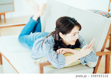 ソファーでスマホを操作する女性。 108593128