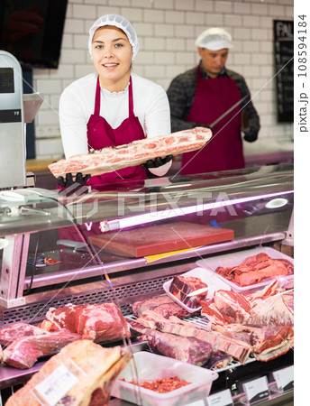 Young female butcher showing raw beef ribs at counter Young female butcher showing raw beef ribs at counter 108594184