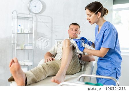 Female doctor performs intra-articular injection treatment of knee bursitis to man patient Female doctor performs intra-articular injection treatment of knee bursitis to man patient 108594238