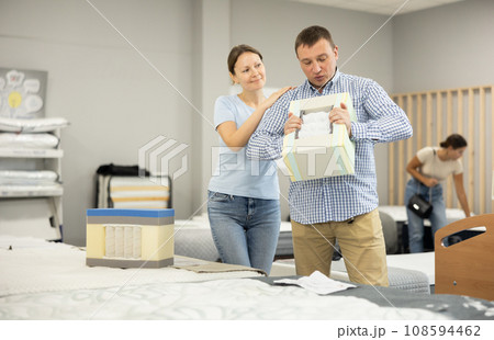 Married couple chooses and discusses mattress filling in furniture store 108594462