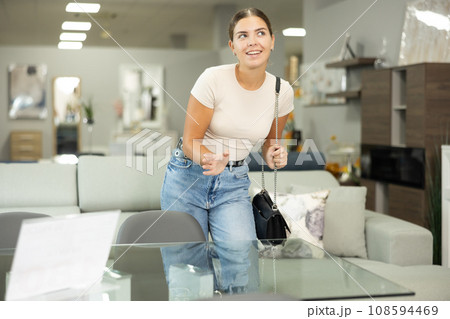 Girl buyer choose dining table desk in furniture store showroom Girl buyer choose dining table desk in furniture store showroom 108594469