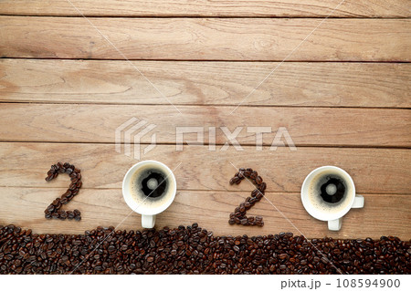 Top view of coffee beans and hot fresh coffee in a white cup with foam and text number design 2024 for Happy New Year Concept. on wooden table background. Top view of coffee beans and hot fresh coffee in a white cup with foam and text number design 2024 for Happy New Year Concept. on wooden table background. 108594900
