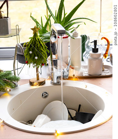 Dirty dishes in the sink in the garlanded kitchen, a holiday after a feast at Christmas. Mess after the guests for the New Year, kitchen cleaning, detergent, cleaning services Dirty dishes in the sink in the garlanded kitchen, a holiday after a feast at Christmas. Mess after the guests for the New Year, kitchen cleaning, detergent, cleaning services 108602801