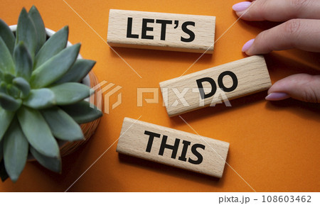 Lets do this symbol. Concept word Lets do this on wooden blocks. Businessman hand. Beautiful orange background with succulent plant. Business and Lets do this concept. Copy space 108603462