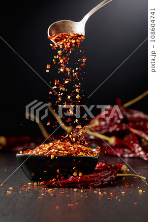 Chilli flakes are poured into a black dish. Chilli flakes are poured into a black dish. 108604741