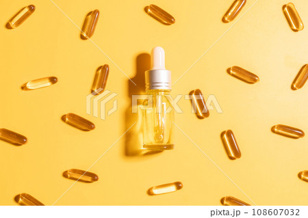 Oil capsules and serum bottle with dropper on yellow background. Nutritional supplement contains fish oil, omega 3, omega 6, omega 9, vitamin e, vitamin d and vitamin. Health care and beauty concept. Oil capsules and serum bottle with dropper on yellow background. Nutritional supplement contains fish oil, omega 3, omega 6, omega 9, vitamin e, vitamin d and vitamin. Health care and beauty concept. 108607032