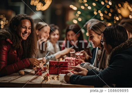 two women sitting at a table with christmas lights in the background and one woman holding a red box that says happy new year 108609895