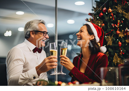a man and woman holding champagne flutes in front of a christmas tree with lights on the wall behind them they are smiling at each 108610164