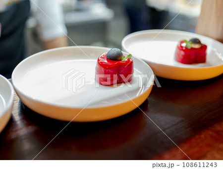 Red heart dessert on white plate with black chocolate top. 108611243