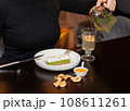 Cropped view of woman in black turtleneck pouring brewed green tea 108611261