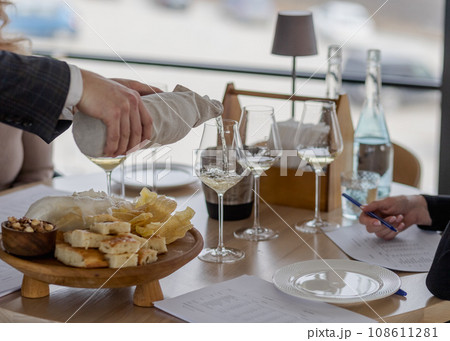 Sommelier pouring white wine into glasses with hidden bottle Sommelier pouring white wine into glasses with hidden bottle 108611281