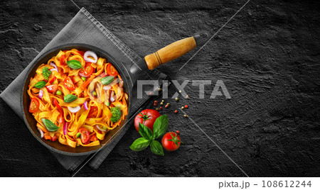 Tasty Pasta noodles linguine in tomato sauce with vegetables in pan on black stone background. 108612244