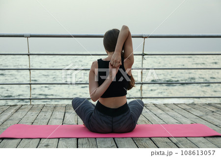 Woman on yoga mat on wooden floor at sea 108613057