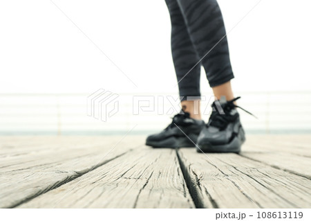 Female legs in leggings and sneakers on wooden floor at sea Female legs in leggings and sneakers on wooden floor at sea 108613119