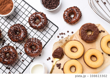 Chocolate donuts, spoon, whisk and bowls on white background, top view 108613302