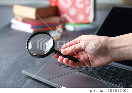 Magnifying glass in hand and laptop on wooden background 108613406