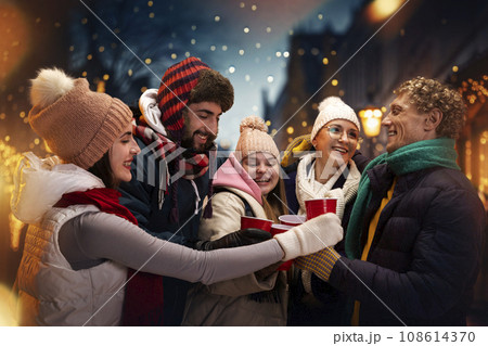 Group portrait of adorable smiling people in cozy fair atmosphere standing outdoor and having fun while drinking hot warming drink. 108614370