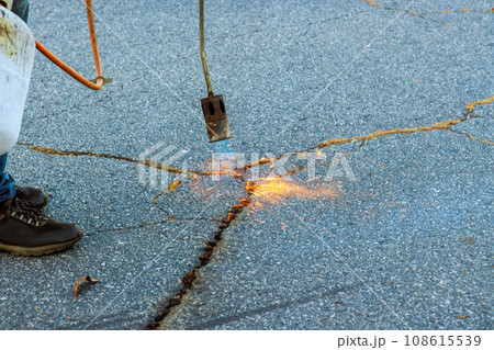 Road surface restoration work in the worker performs on burning dry grass in asphalt cracks before coated bitumen emulsion 108615539