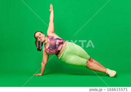 Positive, young overweigh woman training, standing in plank position against green studio background. Sport, body-positivity Positive, young overweigh woman training, standing in plank position against green studio background. Sport, body-positivity 108615571