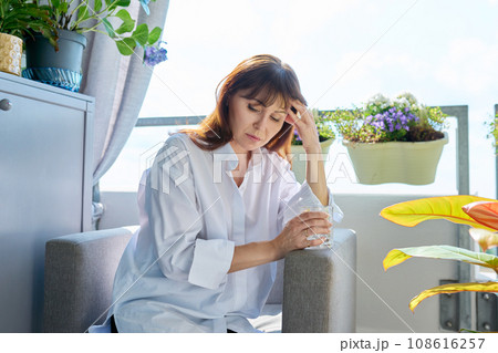 Mature woman suffering from pain, with glass of water at home in chair 108616257