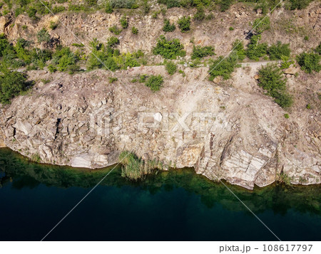 Rocky shore of the Radon Lake on a sunny summer morning. Aerial view of an old flooded granite quarry. A picturesque pond. 108617797
