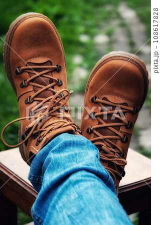Brown boots and jeans on the legs. Legs are crossed on the stool. 108617828