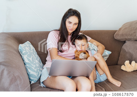 Young Mother and son on the sofa using laptop. Happy mom and little boy hugging and watching videos, reading books, playing video game, using online app, studying together at home. Family time. Young Mother and son on the sofa using laptop. Happy mom and little boy hugging and watching videos, reading books, playing video game, using online app, studying together at home. Family time. 108617870