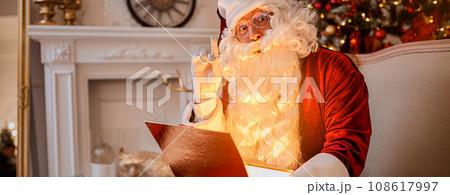 Surprised Santa Claus with glowing gift near christmas tree. New year and Merry Christmas concept Surprised Santa Claus with glowing gift near christmas tree. New year and Merry Christmas concept 108617997
