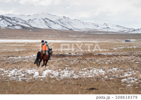 Two children riding a horse, view from the back. A yurt on a snowy plateau, nomadic life in Mongolia. A wide expanse. 108618379