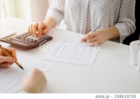 Two accountants using a calculator and laptop computer for counting taxes at white desk in office. Teamwork in business audit and finance Two accountants using a calculator and laptop computer for counting taxes at white desk in office. Teamwork in business audit and finance 108618791