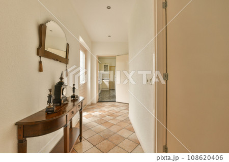 a hallway with a mirror on the wall and an open door leading to another room that has a tiled floor 108620406