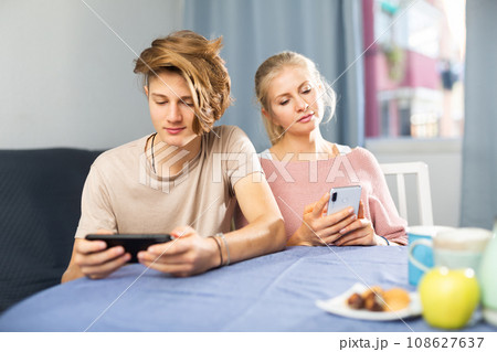 Teenage boy and his mother sitting at home table with smartphones 108627637