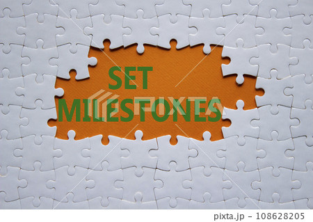 Set milestones symbol. Concept word Set milestones on white puzzle. Beautiful orange background. Business and Set milestones concept. Copy space Set milestones symbol. Concept word Set milestones on white puzzle. Beautiful orange background. Business and Set milestones concept. Copy space 108628205