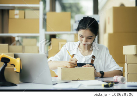 Online business owner writing customer address on a parcel box before shipping 108629506