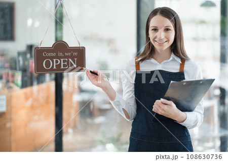 Starting and opening a small business, a young Asian woman showing a smiling face in an apron standing in front of a coffee shop bar counter. Business Owner, Restaurant, Barista, Cafe, Online SME. 108630736