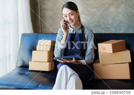 Starting small business entrepreneur of independent Asian female online seller talking on the phone with a customer and packing products for delivery to the customer. and SME delivery concept. Starting small business entrepreneur of independent Asian female online seller talking on the phone with a customer and packing products for delivery to the customer. and SME delivery concept. 108630756