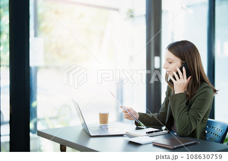 Portrait of a young Asian man showing a smiling face as she uses his phone, computer and financial documents on her desk in the early morning hours. Portrait of a young Asian man showing a smiling face as she uses his phone, computer and financial documents on her desk in the early morning hours. 108630759