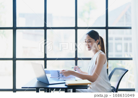 Portrait of a thoughtful Asian businesswoman looking at financial statements and making marketing plans using a computer on her desk. 108631049
