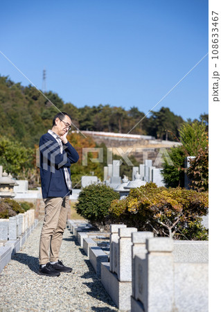 お墓の前で困った顔をして考え込んでいる中高年男性 108633467