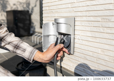 一戸建て住宅の屋外コンセントで車の充電をしている男性 108633737