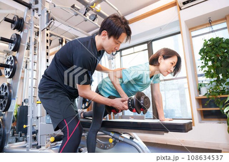 スポーツジムで運動する女性とトレーナー(ダンベル) スポーツジムで運動する女性とトレーナー(ダンベル) 108634537