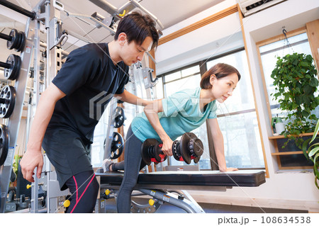 スポーツジムで運動する女性とトレーナー(ダンベル) スポーツジムで運動する女性とトレーナー(ダンベル) 108634538
